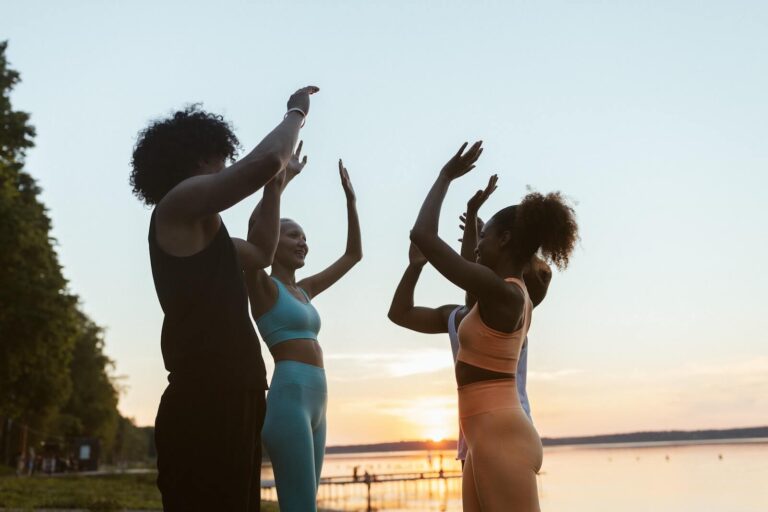 Group of women in exercise clothes standing in a circle outside high fiving