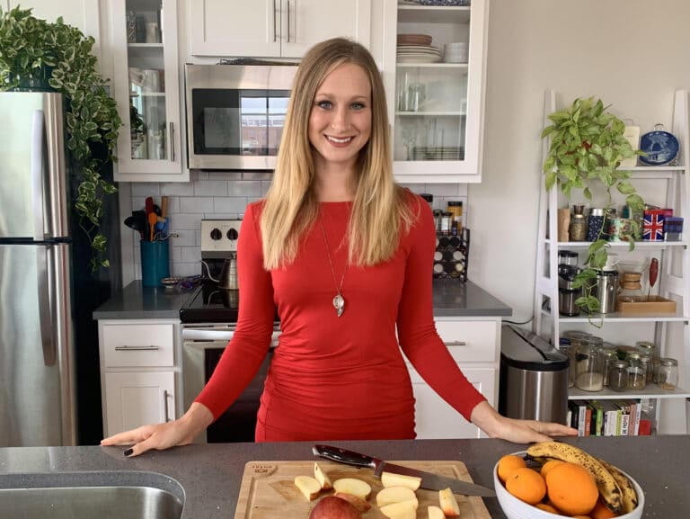 Kaytee standing in the kitchen smiling in front of a cutting board and fruit